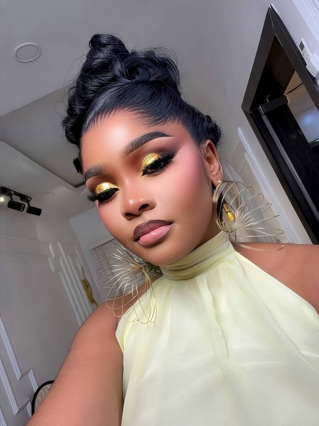 Chioma in a chartreuse halter dress with gold eyeshadow and sculptural gold earrings